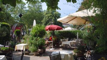 An outdoor patio area with tables and chairs, surrounded by potted plants and umbrellas.