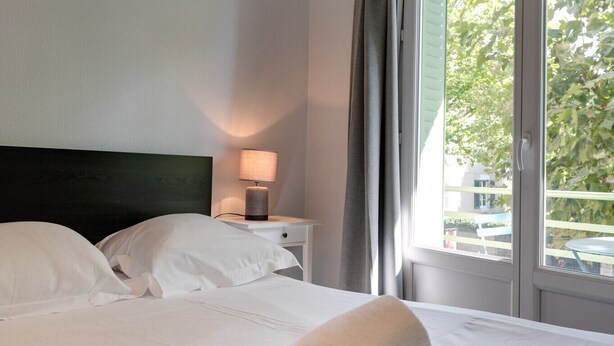 A neatly made bed with white linens, a rolled towel, and a bedside lamp on a nightstand. - 🎖 Le Baulier - 2 bedrooms apartment (Annecy)