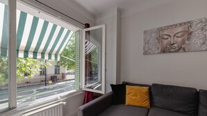 A modern living room with a grey sofa, a window with a striped awning, and a Buddha painting on the wall. - 🎖 Le Baulier - 2 bedrooms apartment (Annecy)