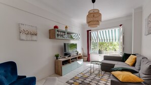 A living room with a sofa, a blue armchair, a TV, a wooden cabinet, and a patterned rug. - 🎖 Le Baulier - 2 bedrooms apartment (Annecy)