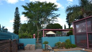 A swimming pool with a tiled deck, surrounded by a brick wall and a blue fence. - Africa Emerald at 47 Petronella (Kempton Park)