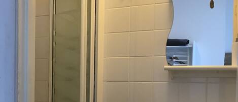 A bathroom with a glass shower door, a sink with a mirror above it, and a towel rack on the wall.