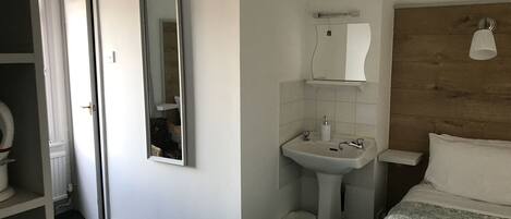 Una habitación de hotel con cama, mesita de noche, espejo, lavamanos y retrete.