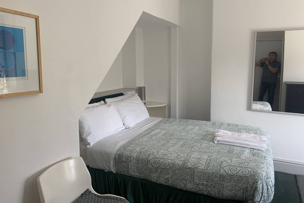 A hotel room with a bed, a chair, a mirror, and a framed picture on the wall.