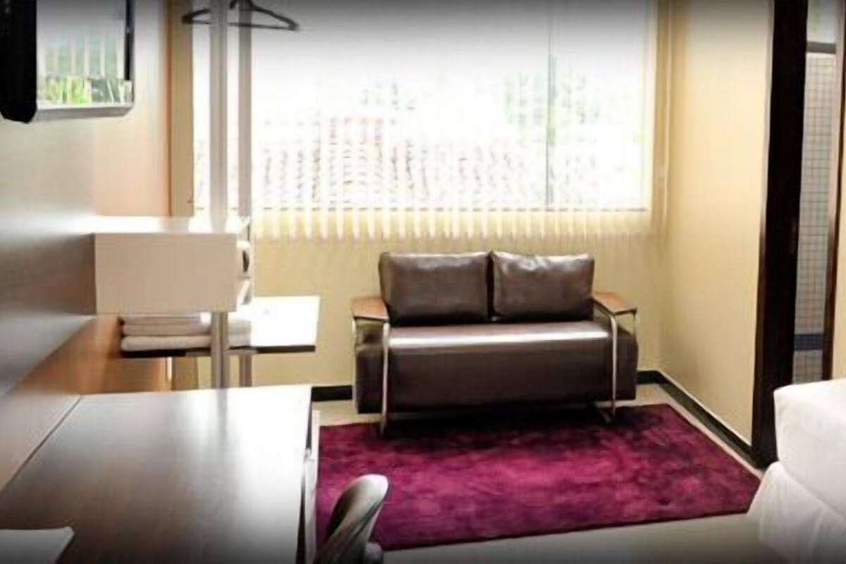 Ein Hotelzimmer mit einem Bett, einem Schreibtisch, einem Sessel und einer kleinen Couch, sowie einem Fenster mit Jalousien.