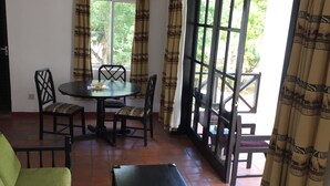 Un comedor con una mesa y sillas, un banco y un sofá. Hay una ventana con cortinas y vistas a la vegetación.