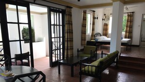 Una habitación con una cama, un escritorio, una silla, una mesa y un sofá. Hay una ventana con cortinas, una puerta y una escalera que conduce a otra habitación.