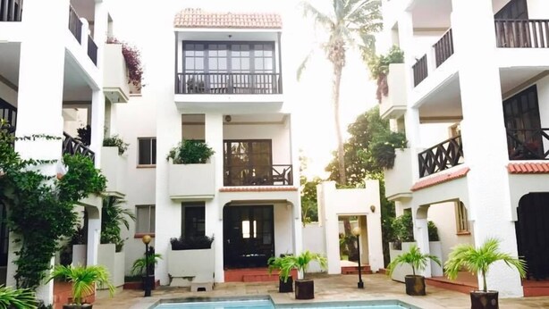 Un patio con piscina, rodeado de edificios blancos con balcones y plantas en macetas.