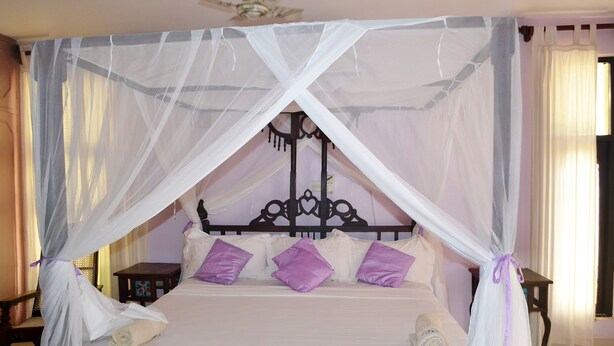 Ein Himmelsbett mit Holzrahmen, weißer Bettwäsche und violetten Kissen.