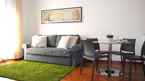 A modern living room with a grey sofa, a green rug, a dining table with chairs, and a painting on the wall. - BNBOOK-RESIDENZA NAGGI (CASORATE SEMPIONE)