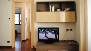 A living room with a flat-screen TV on a wooden stand, a bookshelf above, and a door leading to another room. - BNBOOK-RESIDENZA NAGGI (CASORATE SEMPIONE)