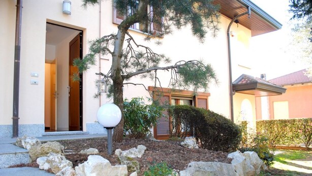 A building entrance with a stone pathway, a tree, and a small garden area. - BNBOOK-RESIDENZA NAGGI (CASORATE SEMPIONE)