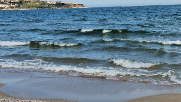 A beach with waves and a distant shoreline with buildings. - Casa de Oro Aparthotel (Sozopol)