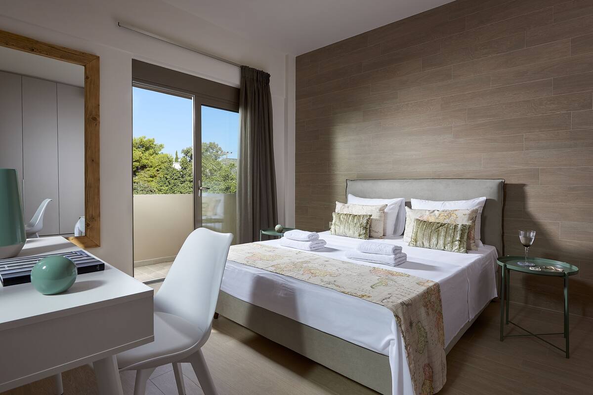 Een hotelkamer met een bed, een bureau, een stoel, een klein tafeltje en een raam met gordijnen.