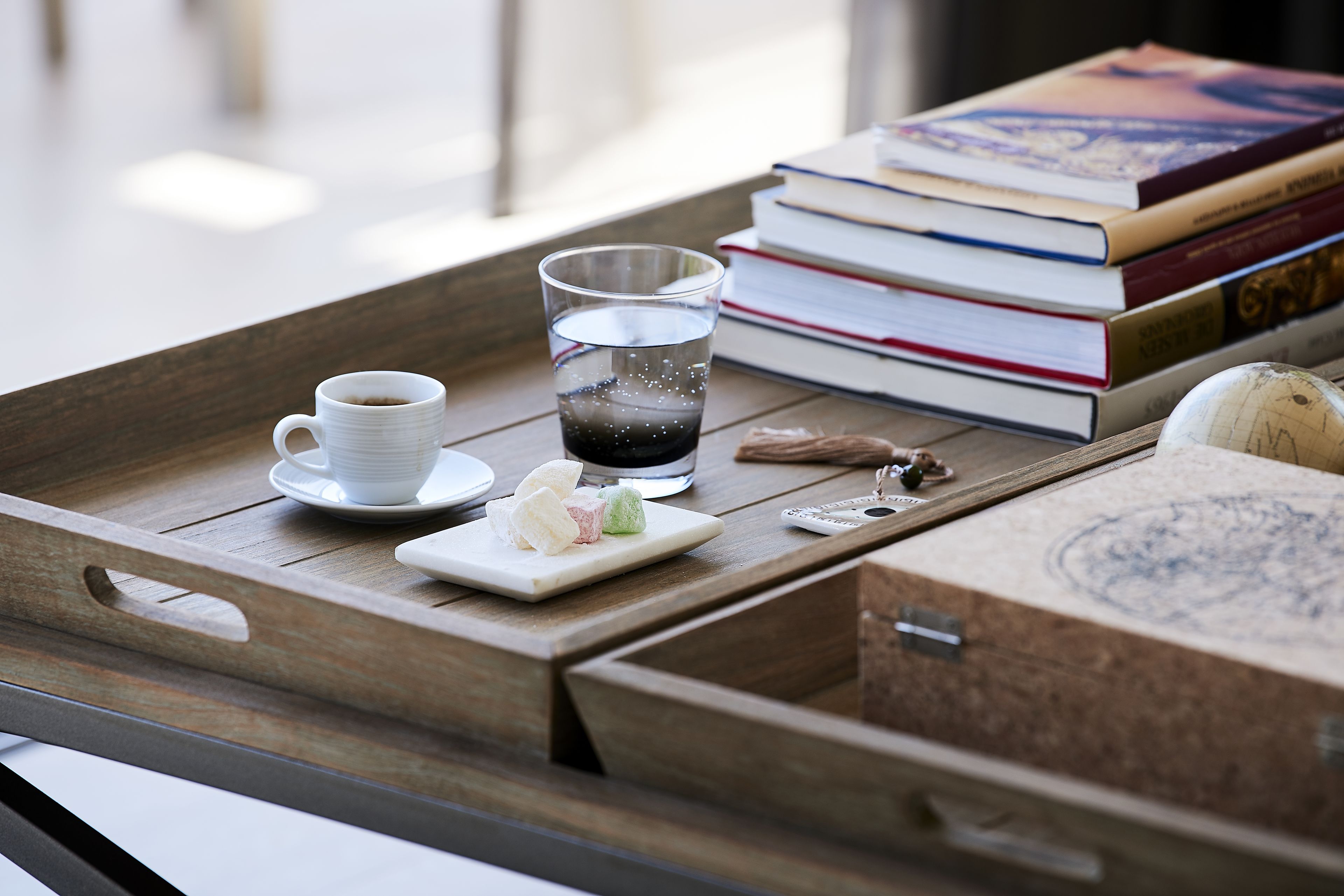 Un plateau en bois avec une tasse de café, un verre d’eau, une assiette de friandises, une pile de livres et un globe terrestre.