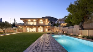 Una casa moderna de dos pisos amb piscina, gespa ben cuidada i una muntanya al fons.