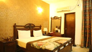 A traditional bedroom with a wooden bed, a nightstand, a mirror, and an air conditioning unit on the wall. - Hotel Sweet Inn (Lahore)