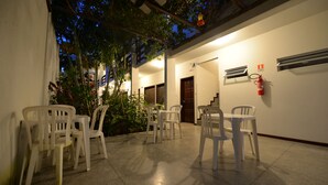 Une terrasse extérieure avec des chaises et des tables en plastique blanc, un extincteur fixé au mur et un escalier menant à un niveau supérieur.