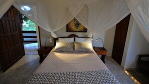 Une chambre à coucher avec un lit, deux tables de chevet, une commode, une porte en bois et une vue sur un jardin.