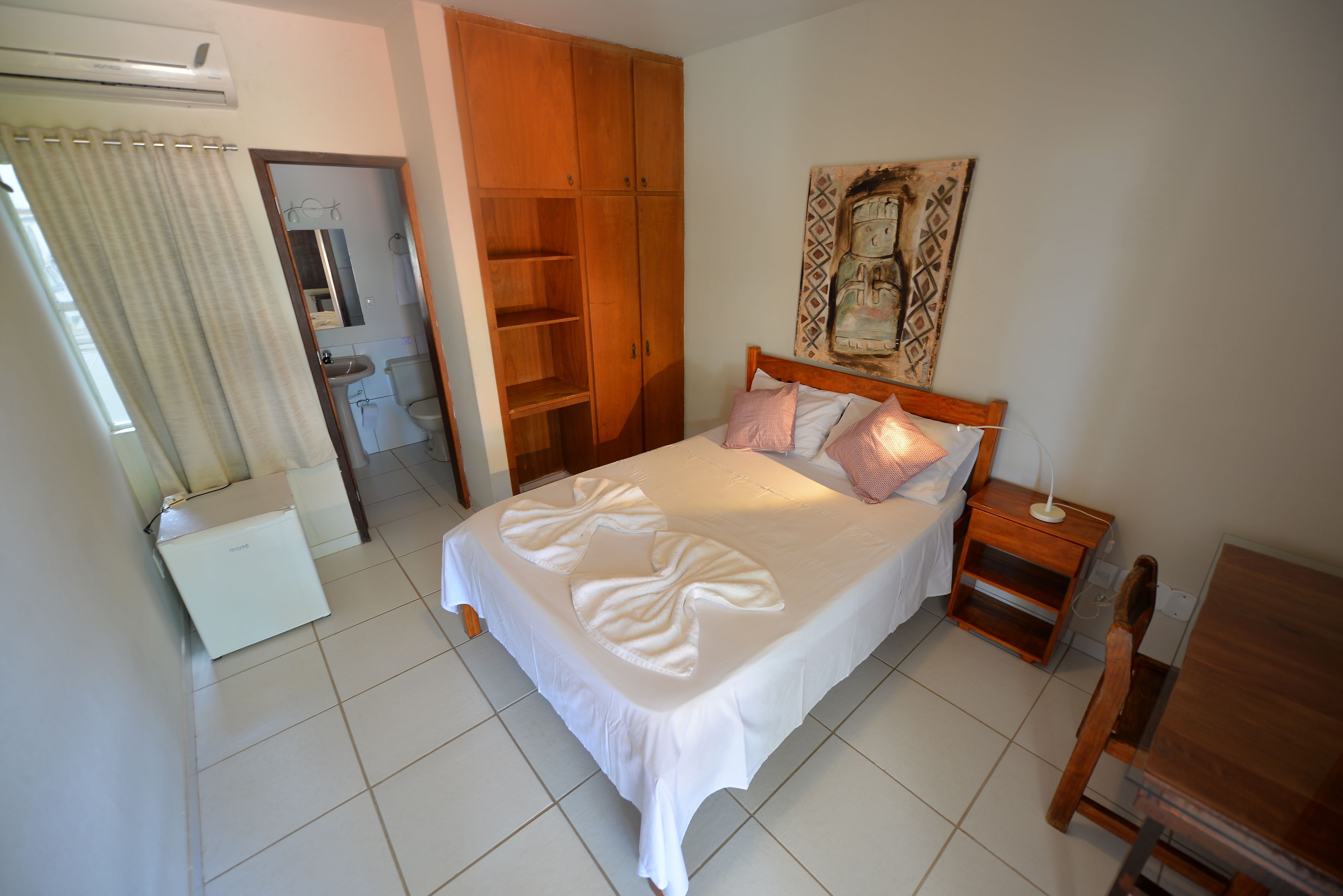 A bedroom with a bed, a wooden wardrobe, a bedside table, and a bathroom visible through an open door.