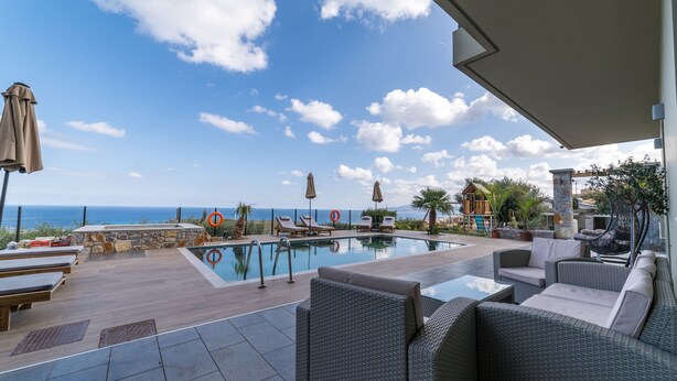 A poolside area with lounge chairs, a pool, and a view of the ocean. - Villa Constandinos (Hersonissos)