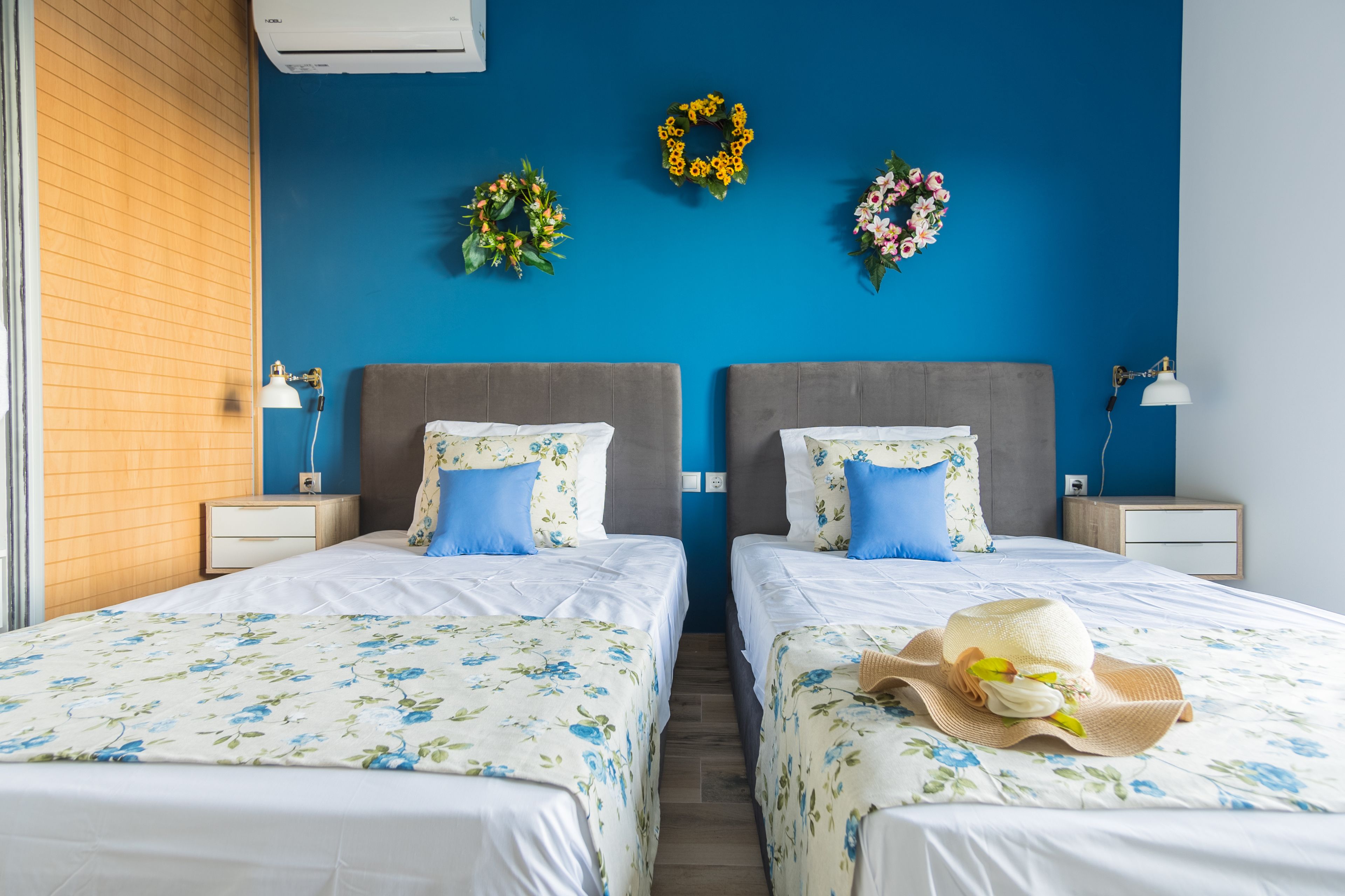 A hotel room with two beds, a blue accent wall, and a decorative wreath.