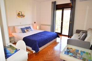 A bedroom with a bed, a bedside table, a chair, a sofa, and a window with curtains. - Elza Apartments (Zadar)