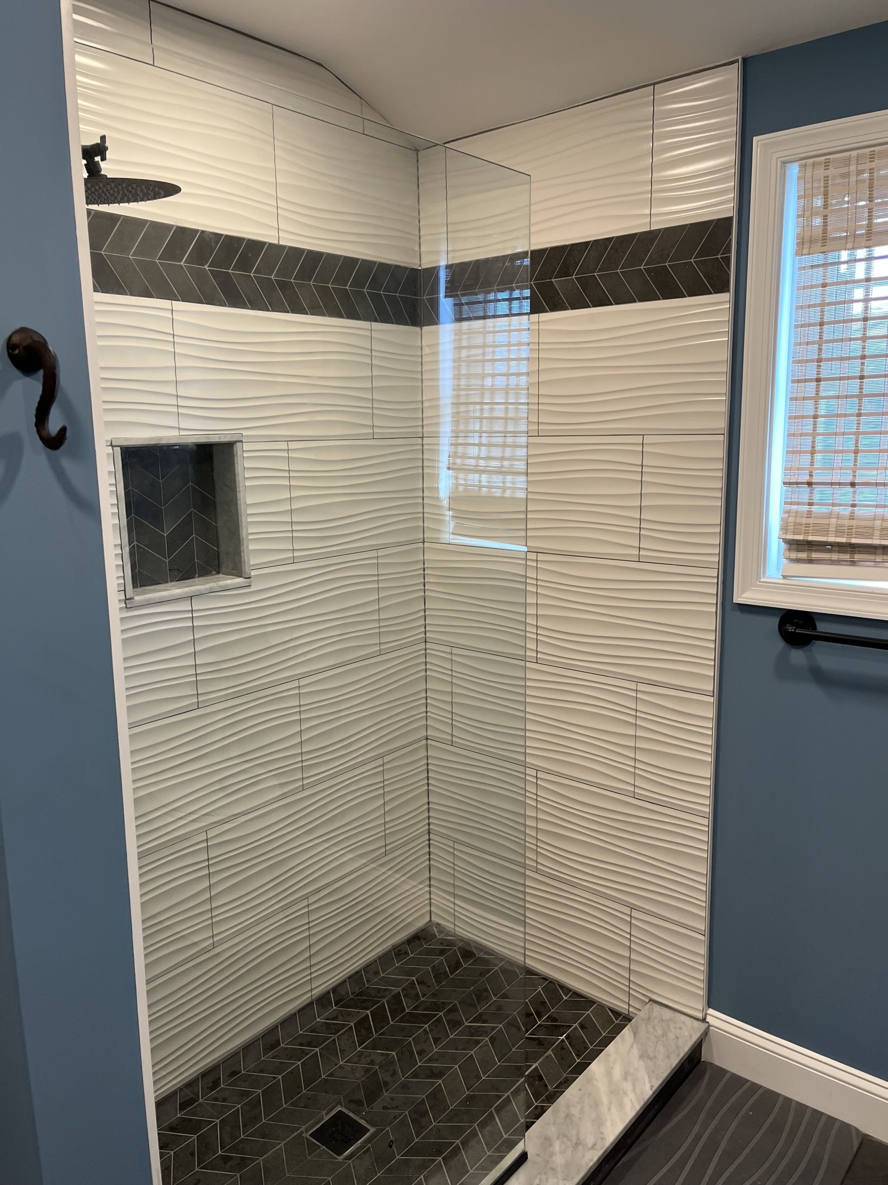 A shower with a unique wavy tile design, a small window, and a handrail.