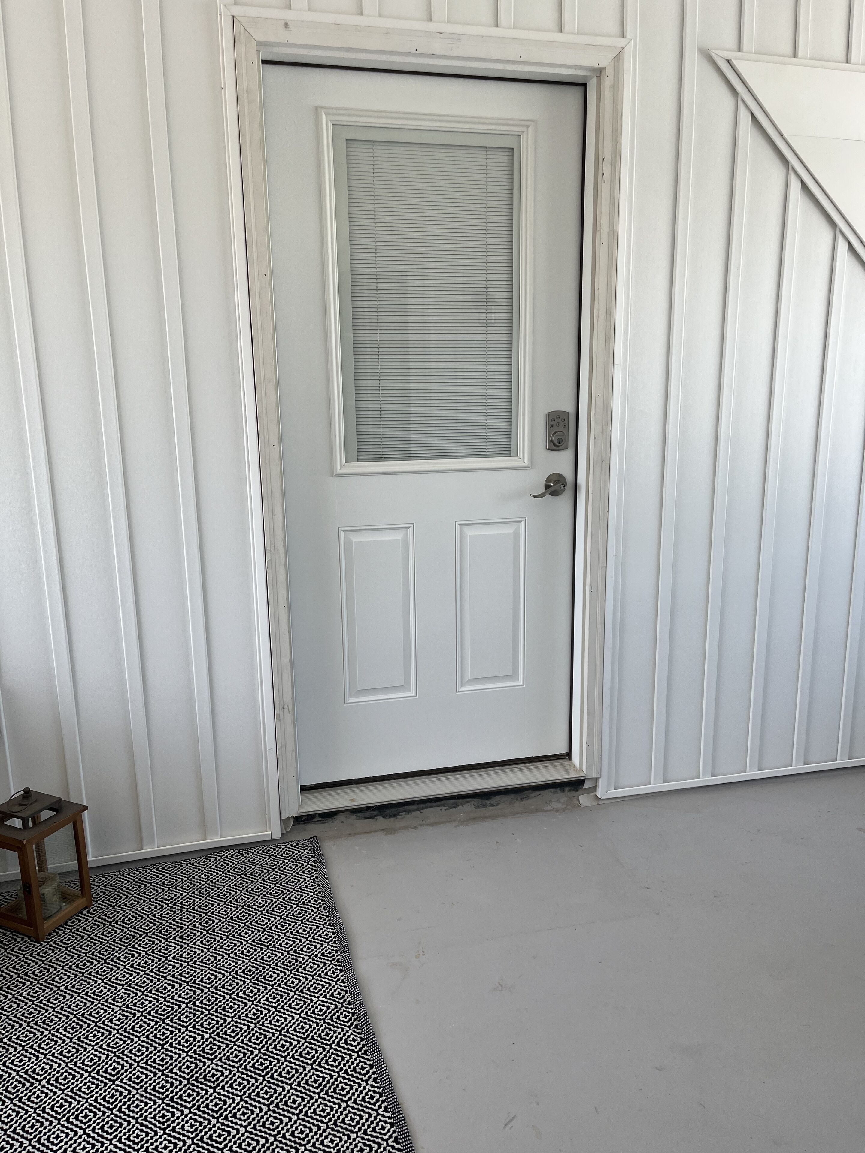 Eine weiße Tür mit Fenster, ein kleiner Podeststufenaufgang davor und ein gemustertes Teppich im Vordergrund.