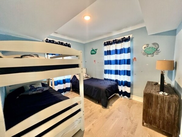 A bedroom with bunk beds, a wooden side table, a lamp, and striped curtains.