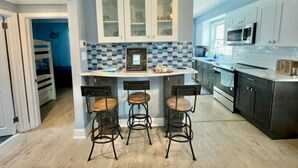 Una cocina moderna con una isla central, taburetes de bar y vista a un dormitorio.