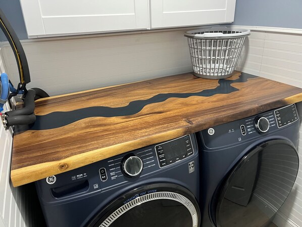 Una lavadora de carga frontal con una encimera de madera y una cesta de ropa encima.