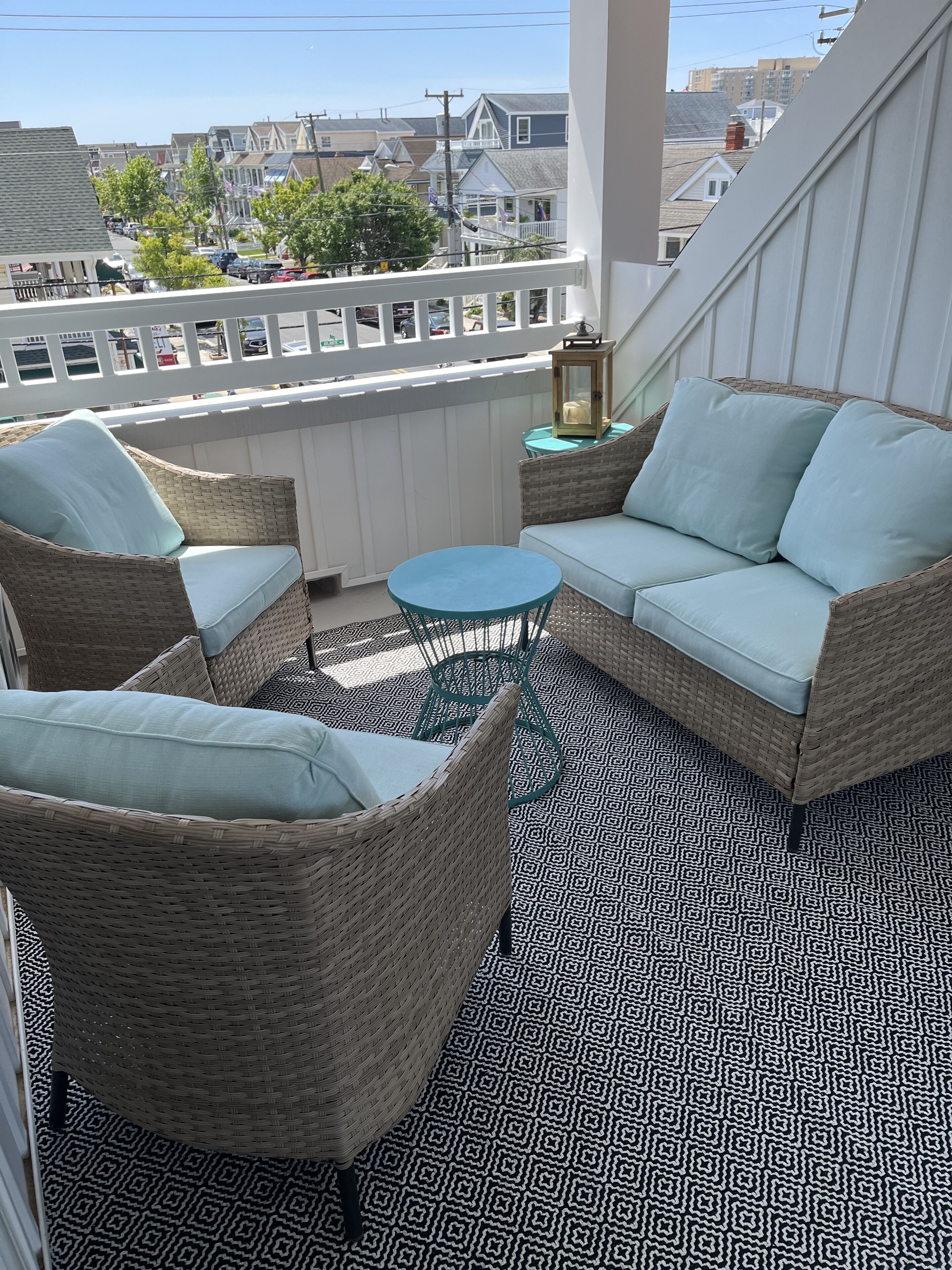 A balcony with wicker furniture, a patterned floor, and a view of buildings in the background.