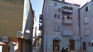Una calle estrecha flanqueada por edificios con balcones, ventanas y un rótulo.