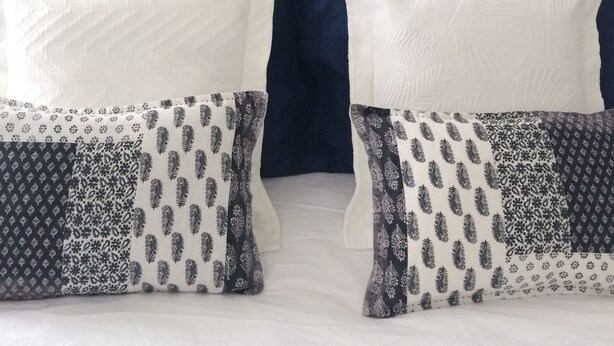 A bed with white and patterned pillows, a blue headboard, and a wall with a simple design.