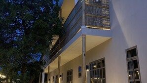 A two-story building with a balcony, large windows, and a tree in the foreground.