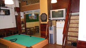 Ein Billardtisch in einem Raum mit Dartscheibe, Fernseher und Kühlschrank.