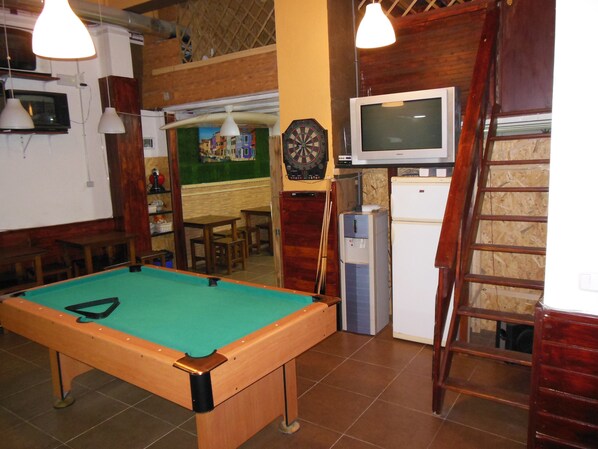 A pool table in a room with a dartboard, a television, and a refrigerator. - Better Oh! Special groups (València)