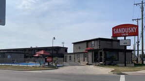 Un Sandusky Inn con un letrero rojo grande, un área de piscina cercada y un estacionamiento.