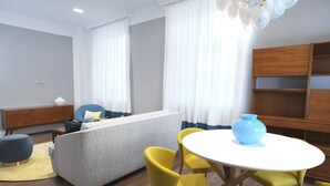 Un salon moderne avec un canapé gris, des fauteuils jaunes, une table blanche et une bibliothèque en bois.