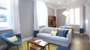 Un salon moderne avec un canapé gris, un fauteuil bleu et un tapis jaune. On y trouve une table basse en bois et un vase bleu posé sur une petite table.
