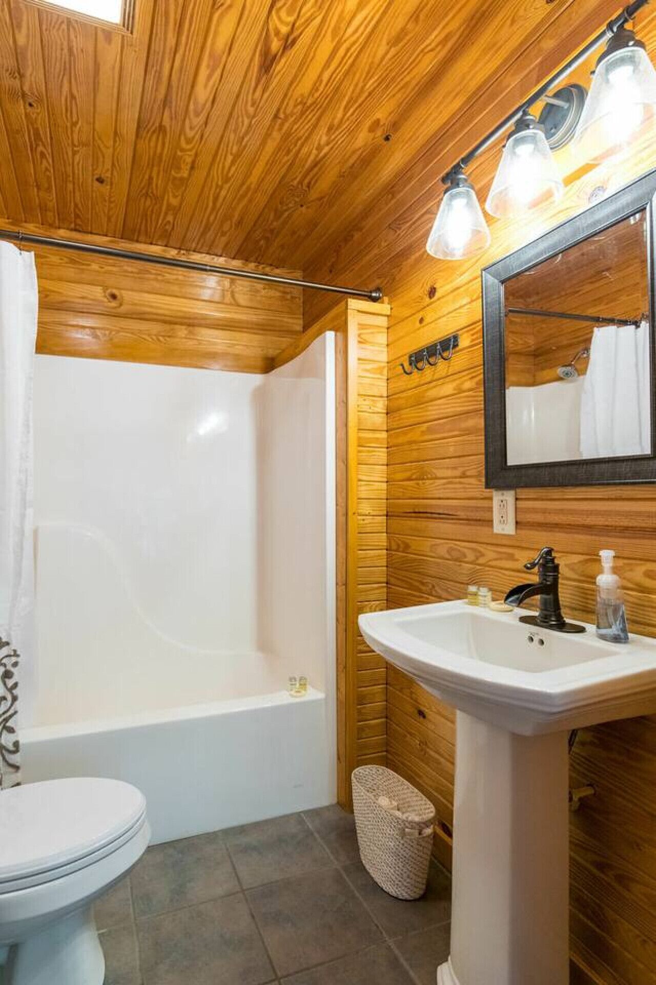 Un bagno con rivestimento in legno, dotato di vasca, water e lavandino.