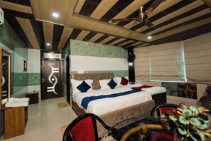 Una habitación de hotel con cama, ventilador de techo, ventana con cortinas y baño con espejo y toallero.