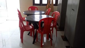 A dining area with a round table and red chairs, an exit sign, and a window with curtains. - Vrinda Palace (Mathura)