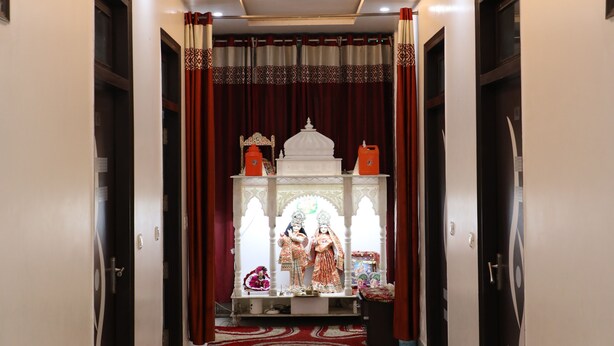 A hallway leading to a room with a shrine, featuring a tiled floor and a door with a decorative handle. - Vrinda Palace (Mathura)