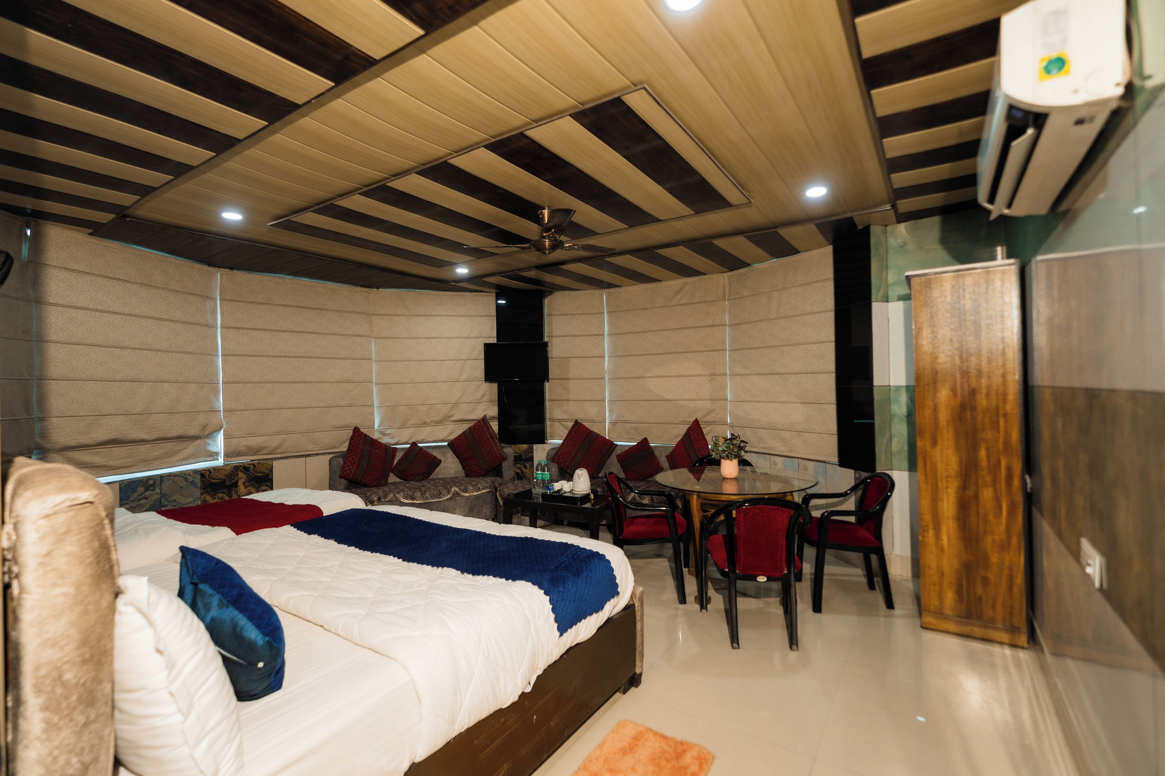 A hotel room with a bed, a dining table with chairs, a TV, and a wardrobe.
