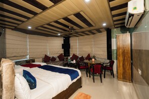 A hotel room with a bed, a dining table with chairs, a TV, and a wardrobe. - Vrinda Palace (Mathura)
