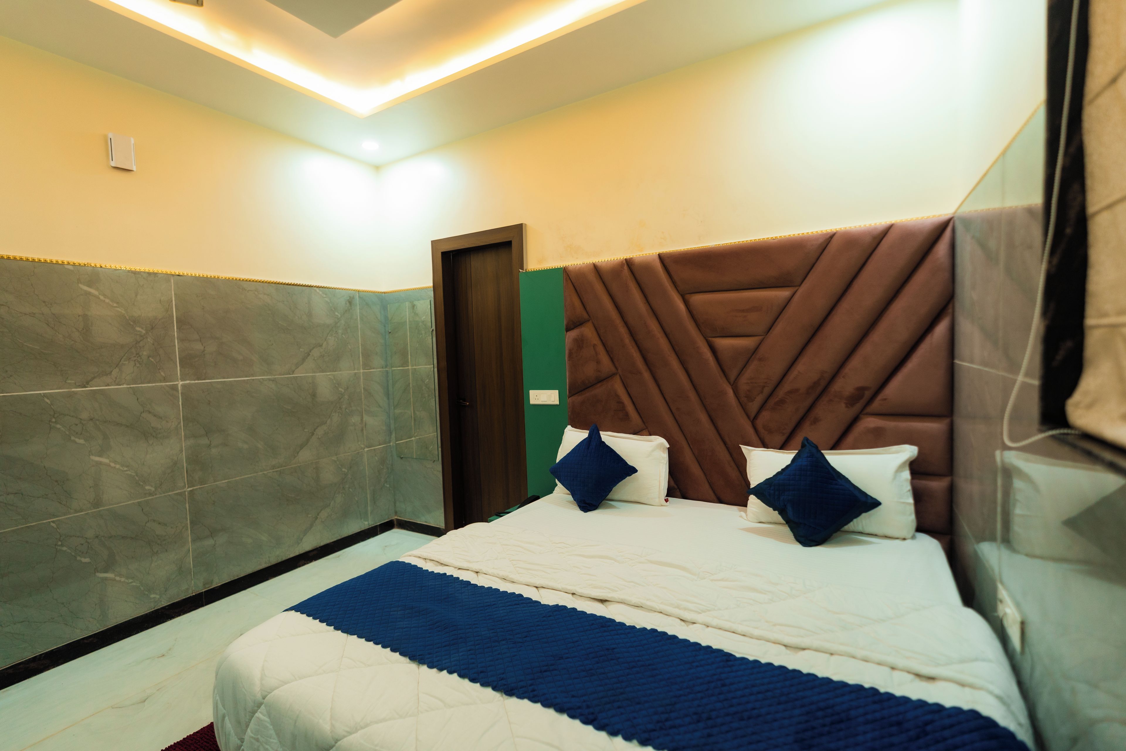 Una habitación de hotel con una cama grande, cabecera de madera y pared con azulejos de mármol.