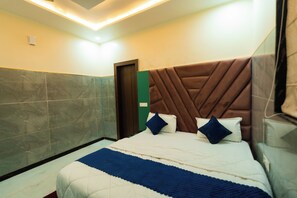A hotel room with a large bed, a wooden headboard, and a marble-tiled wall.