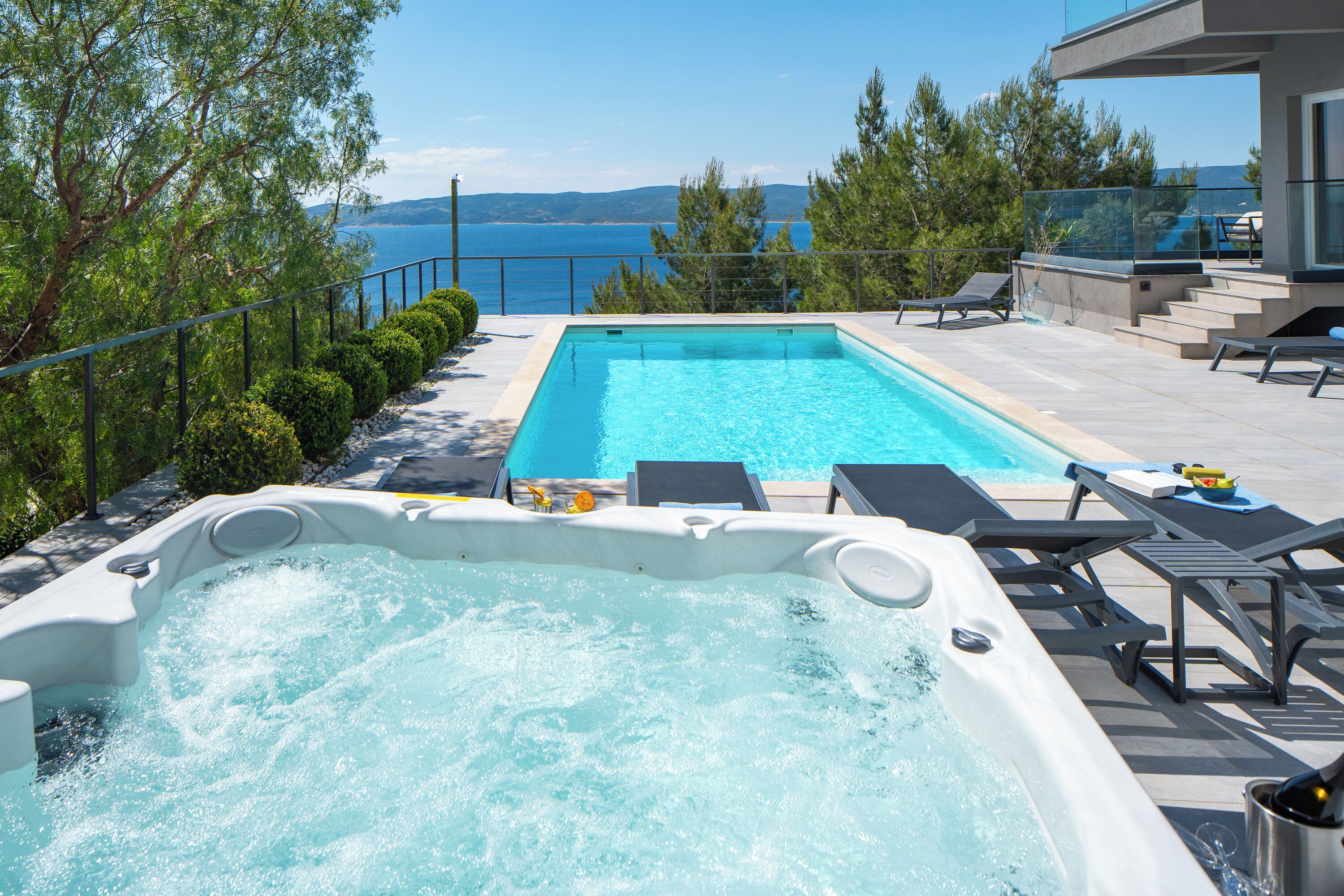 A swimming pool with a hot tub, lounge chairs, and a view of the sea.